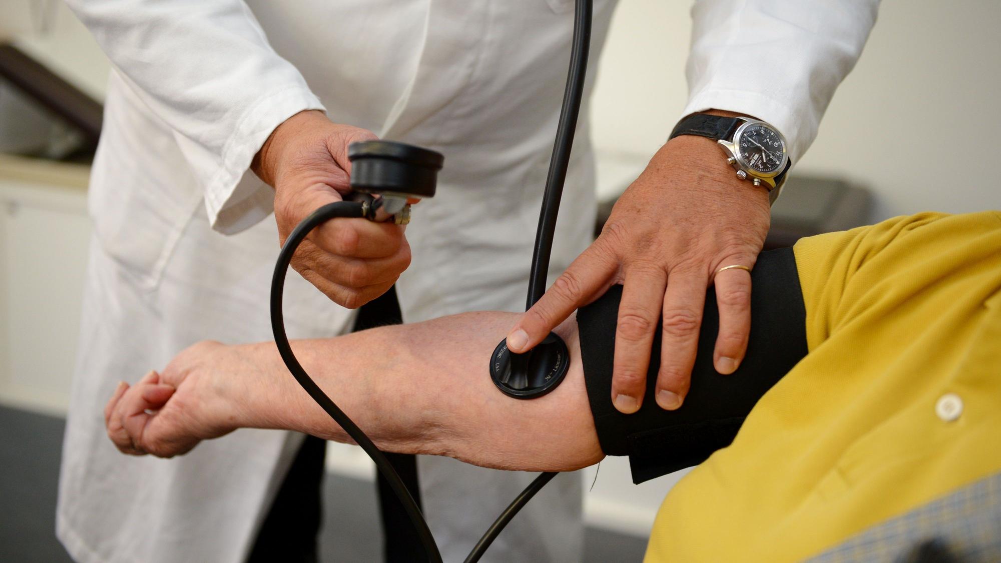 Ein Hausarzt misst in seiner Praxis den Blutdruck einer Patientin.
