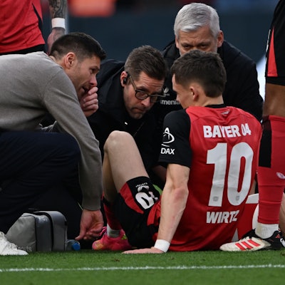 Leverkusens Trainer Xabi Alonso (l) spricht mit Florian Wirtz, der verletzt auf dem Platz sitzt.