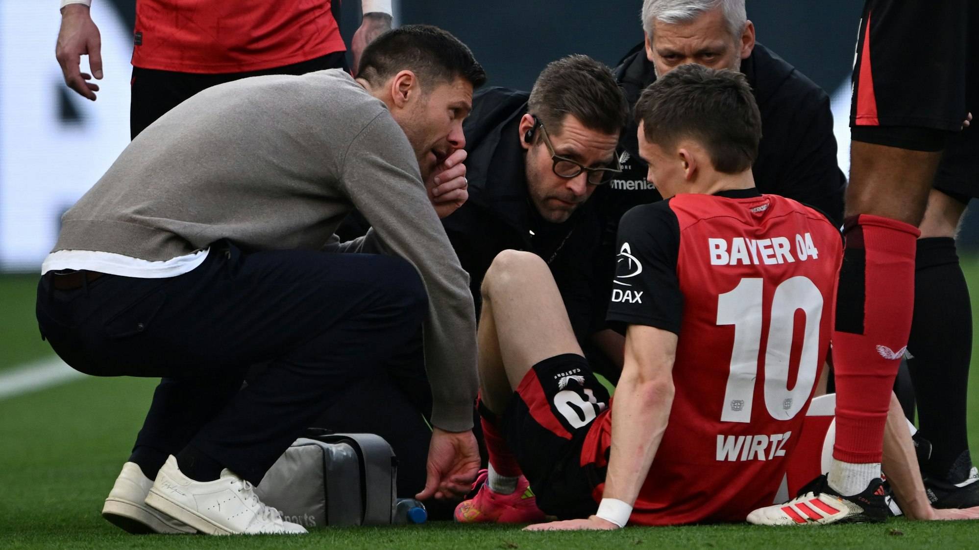 Leverkusens Trainer Xabi Alonso (l) spricht mit Florian Wirtz, der verletzt auf dem Platz sitzt.