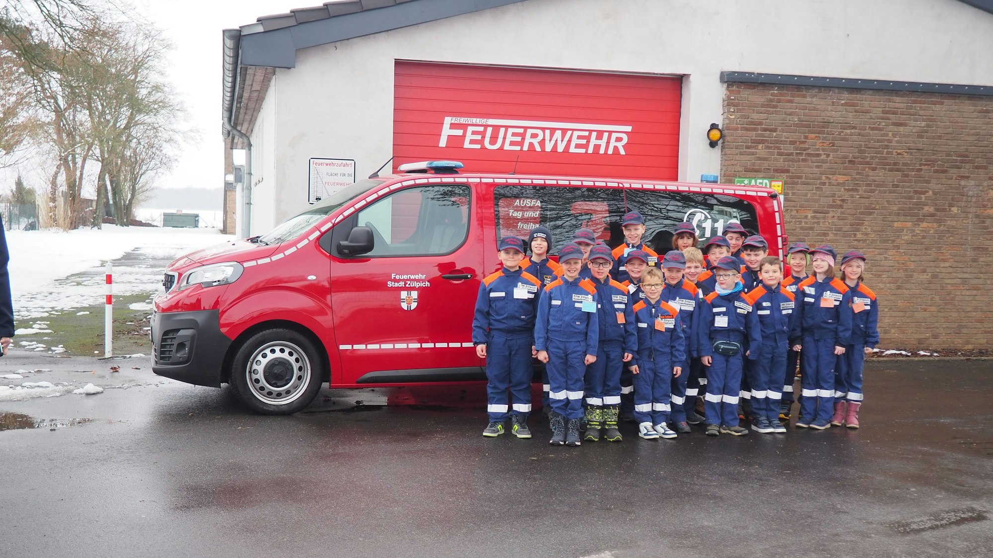 Eine Gruppe Kinder steht in orange-blauen Uniformen vor einem roten Mannschaftstransporter der Feuerwehr.