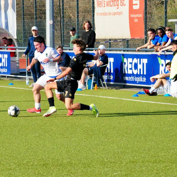 Das Foto zeigt einen Fußballer im weißen Trikot mit Ball am Fuß, der seinem Gegenspieler im schwarzen Dress bedrängt wird.