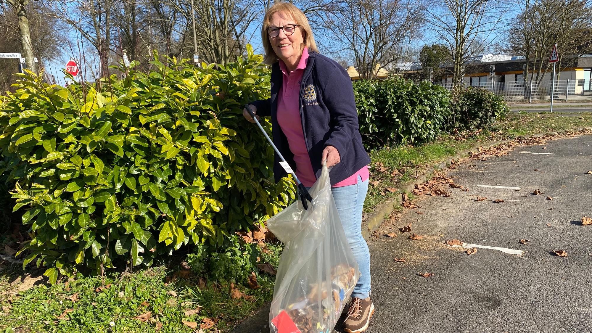 Ein Frau sammelt Müll. Sie hält eine riesige Plastiktüte in der einen und einen Greifzange in der anderen Hand.