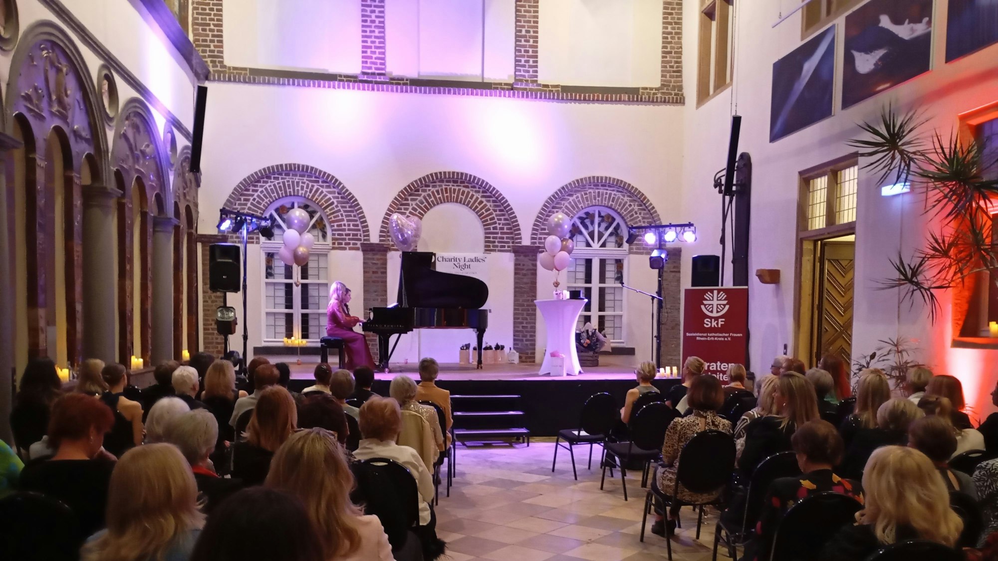 Auf der Bühne steht ein Konzertflügel, violette Ballons sorgen für festliche Stimmung.