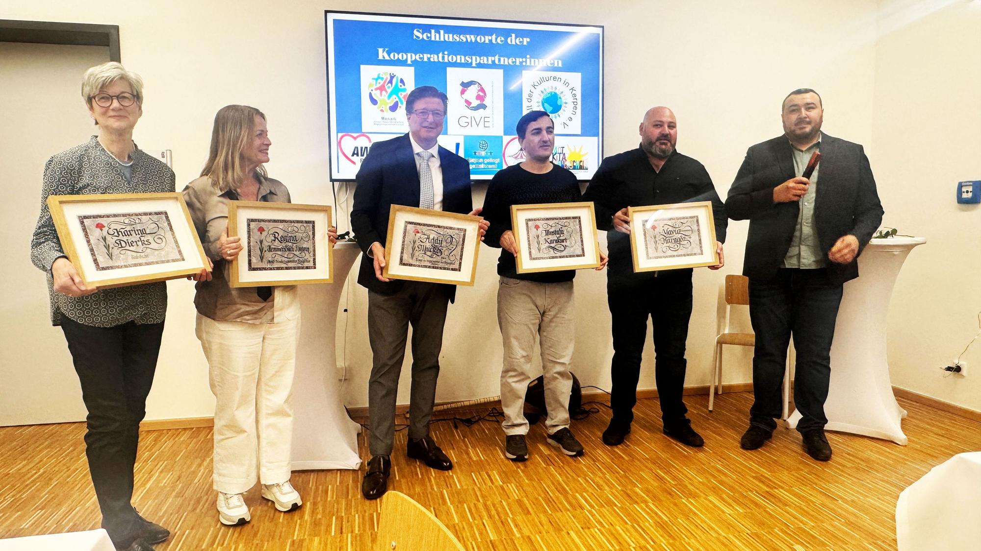 Auf dem Bild stehen Karina Dierks, Regina Hemmersbach-Fontein, Addy Muckes, Mustafa Karakurt, Yavuz Karagöz in einer Reihe und halten Kalligrafien ihres Namens hoch. Daneben steht der Laudator Murat Gök.