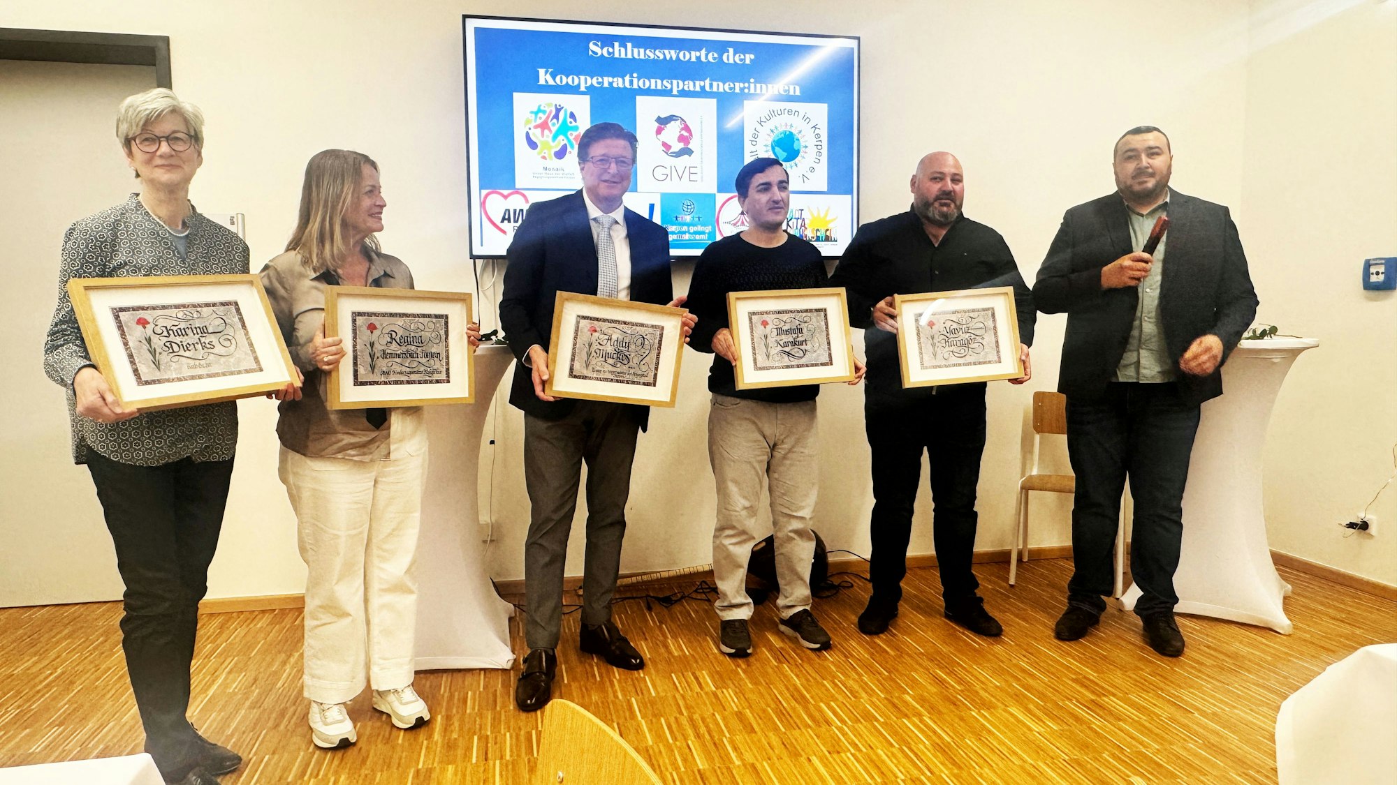 Auf dem Bild stehen Karina Dierks, Regina Hemmersbach-Fontein, Addy Muckes, Mustafa Karakurt, Yavuz Karagöz in einer Reihe und halten Kalligrafien ihres Namens hoch. Daneben steht der Laudator Murat Gök.