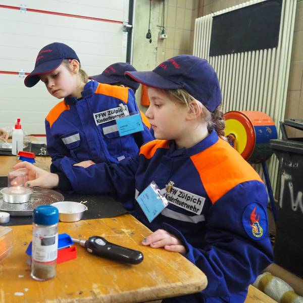 Kinder in orange-blauen Jacken sitzen an einem Tisch und experimentieren.