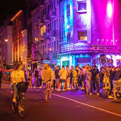 02.06.2021, Köln: Vor dem X3 Corner in der Schaafenstraße stehen zahlreiche Menschen. Nach einem sommerlichen Tag mit warmen Temperaturen sind am späten Abend noch zahlreiche Menschen unterwegs. Einige Einschränkungen zur Eindämmung des Coronavirus wurden in den vergangen Tagen gelockert. Zahlreiche Vorschriften wie Kontaktbeschränkungen gelten aber weiterhin, werden jedoch von vielen ignoriert. Foto: Matthias Heinekamp