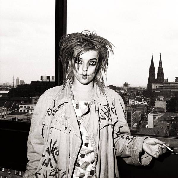 Nina Hagen raucht, den Kölner Dom im Hintergrund, eine Zigarette und zieht dabei die Wangen ein.