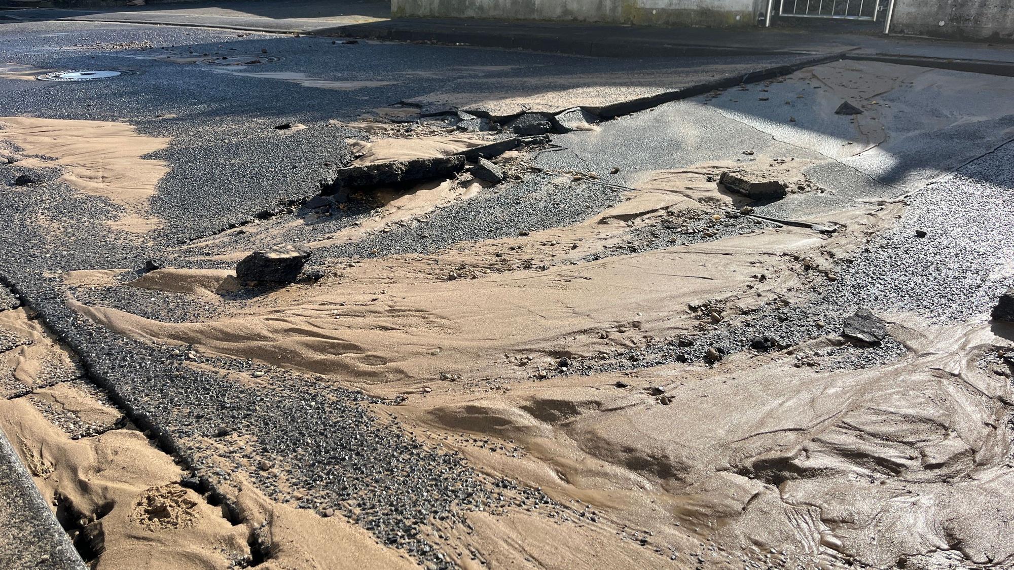 Nach einem Wasserrohrbruch ist der Asphalt aufgebrochen, Schlamm ist auf der Straße verteilt.