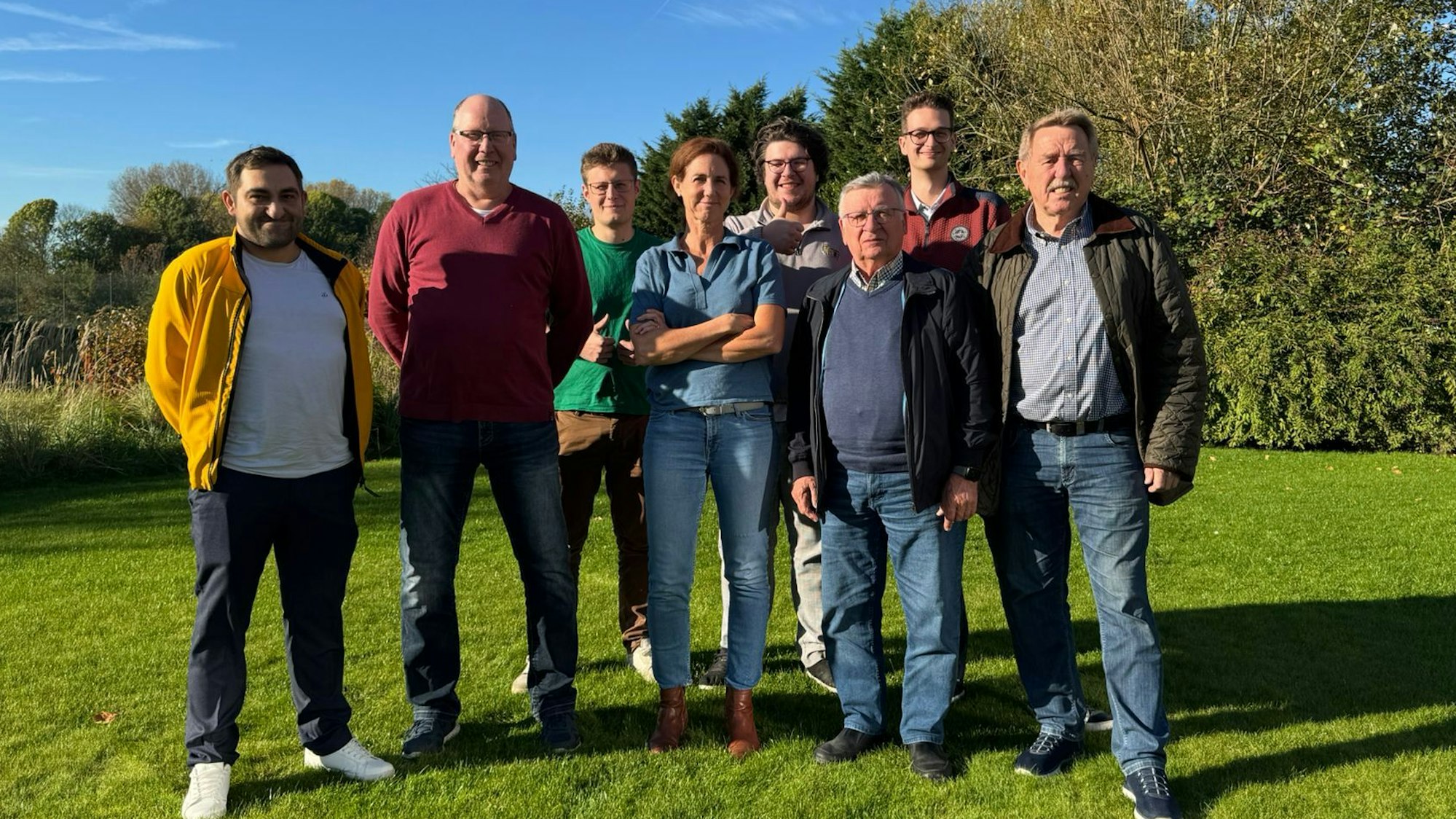 Die Mitglieder stehen in zwei Reihen hintereinander, umgeben von Natur, und schauen in die Kamera.