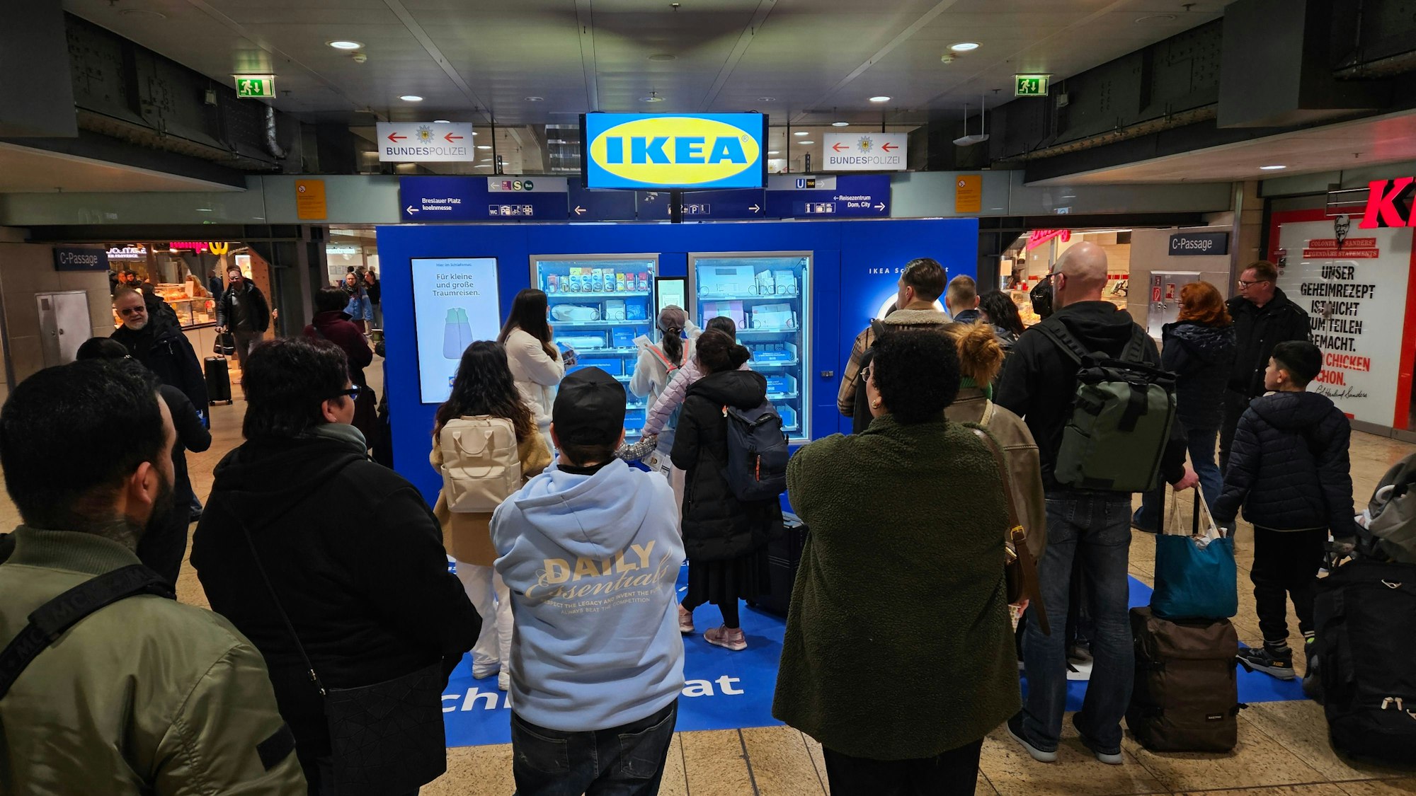 Das Bild zeigt eine Menschenmenge vor dem „Schlafomat“ am Kölner Hauptbahnhof.