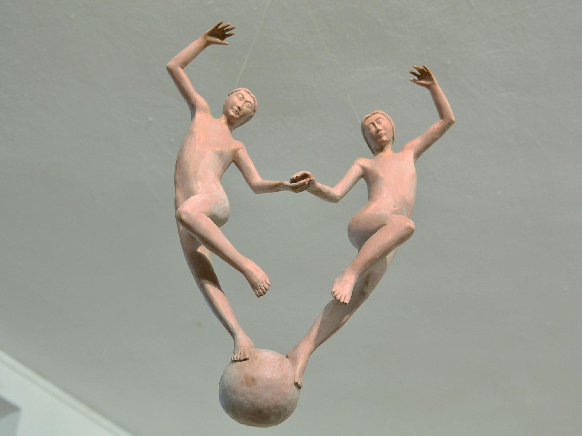 Zwei Figuren, die an hauchdünnen Fäden von der Decke hängen, scheinen auf einer Kugel zu tanzen.