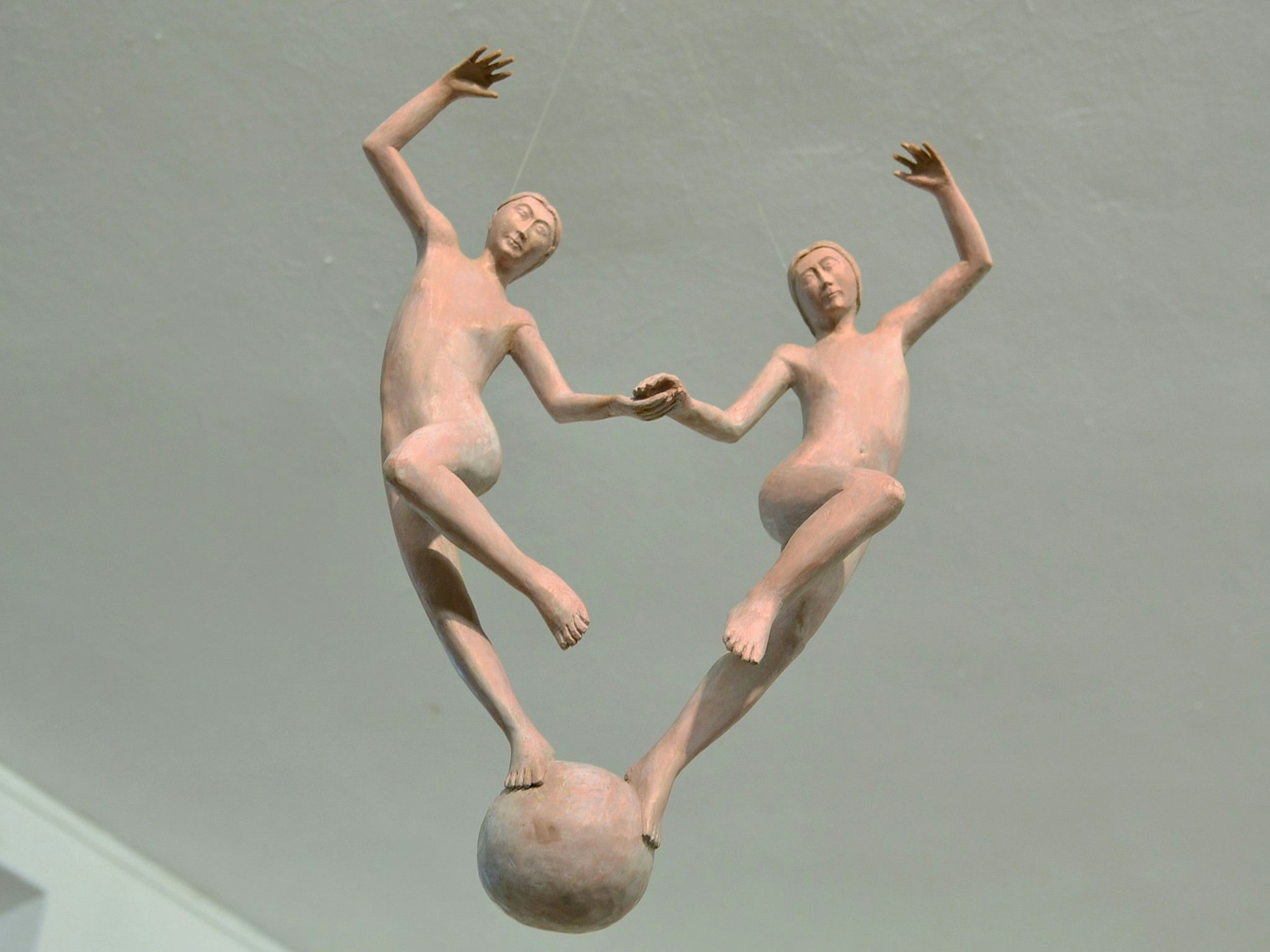 Zwei Figuren, die an hauchdünnen Fäden von der Decke hängen, scheinen auf einer Kugel zu tanzen.