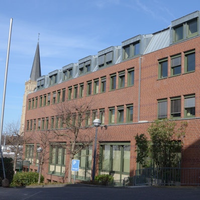 Das Bild zeigt ein Bürogebäude, im Hintergrund die Herz-Jesu-Kirche.