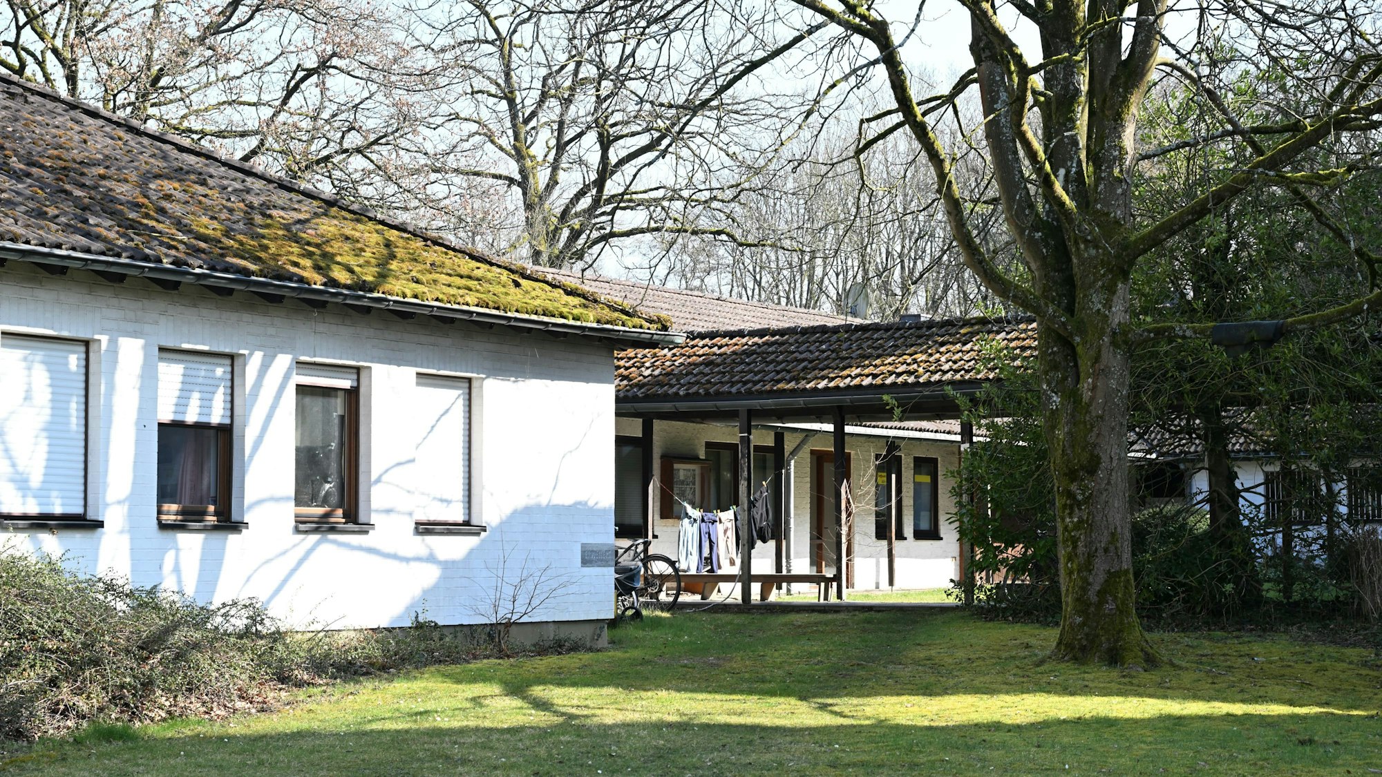 Teile zweier eingeschossiger, weiß gestrichener Nebengebäude sind zu sehen.