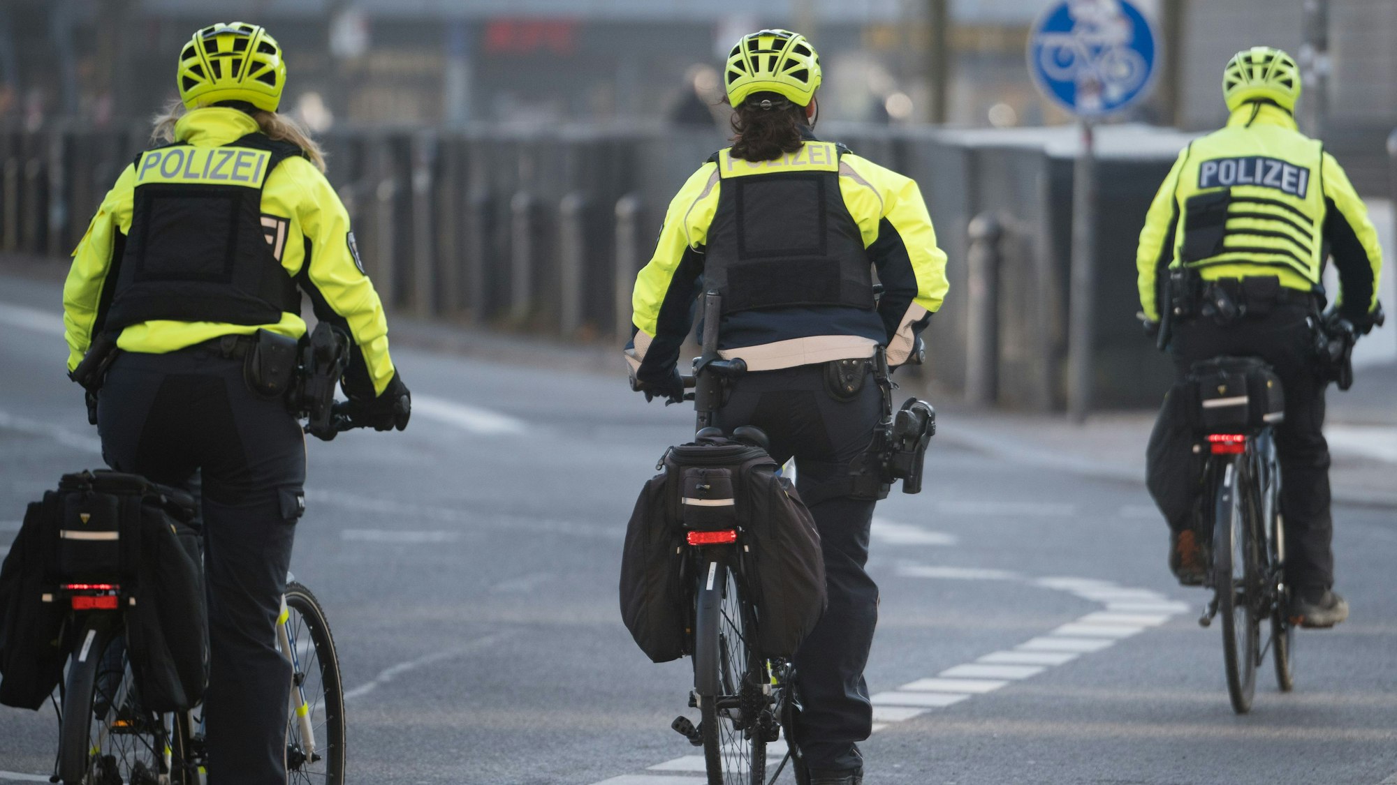 Zu sehen sind drei Polizistinnen und Polizisten in der Rückansicht auf Fahrrädern.