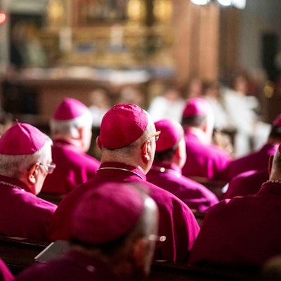 Eine Reihe Bischöfe sitzen in Kirchenbänken.