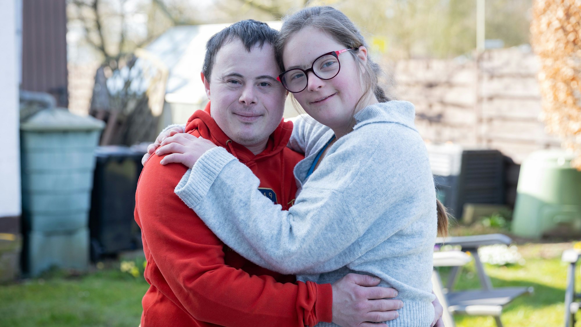 Ein junger Mann mit dunklem Haar und eine junge Frau mit Zopf und Brille halten sich im Arm.