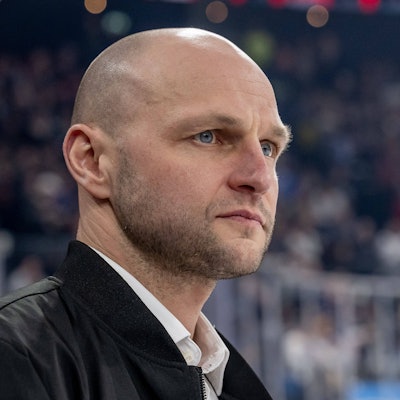 Ein Mann steht in einer Eishockeyhalle und blickt nach vorne.