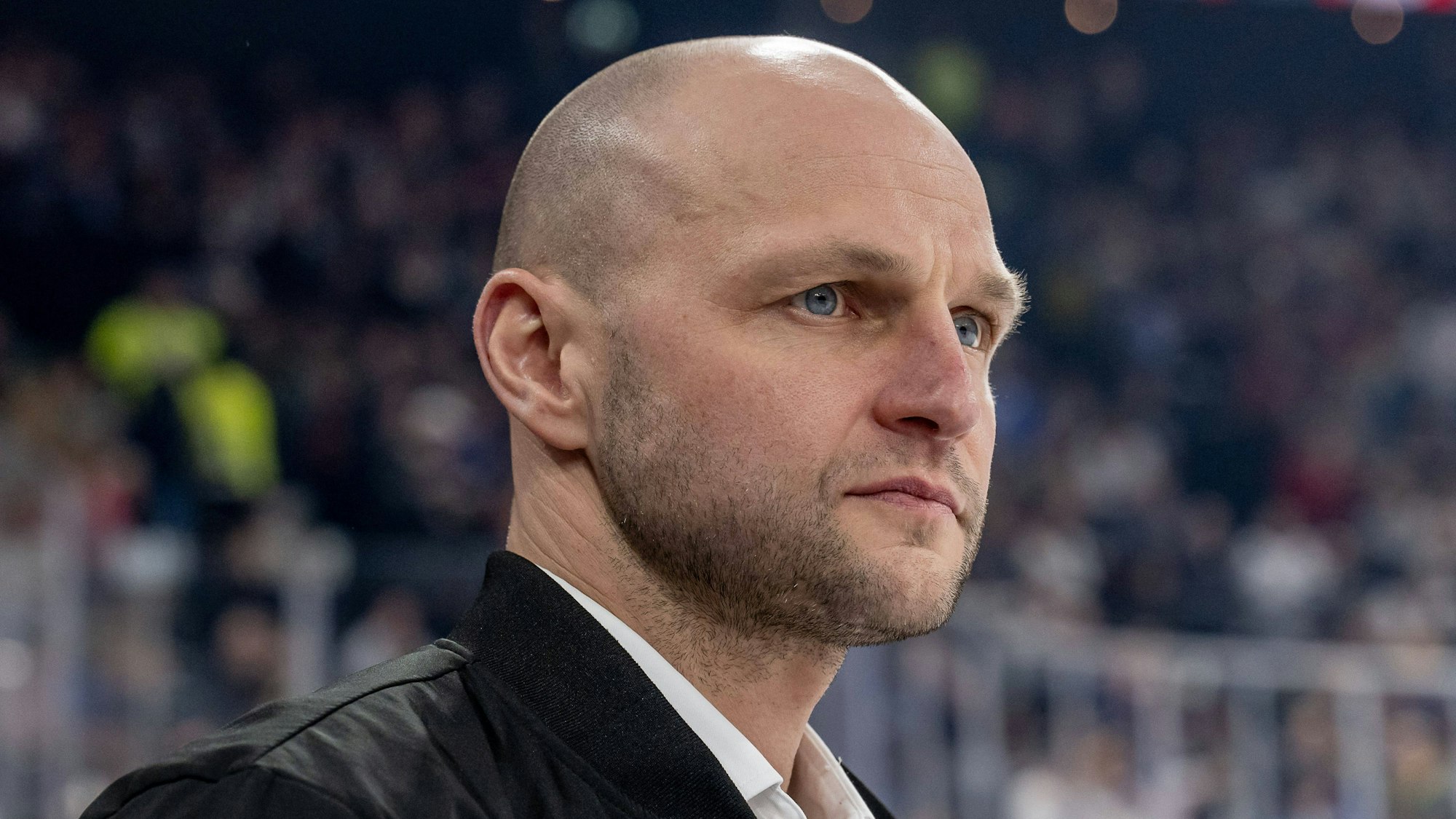 Ein Mann steht in einer Eishockeyhalle und blickt nach vorne.