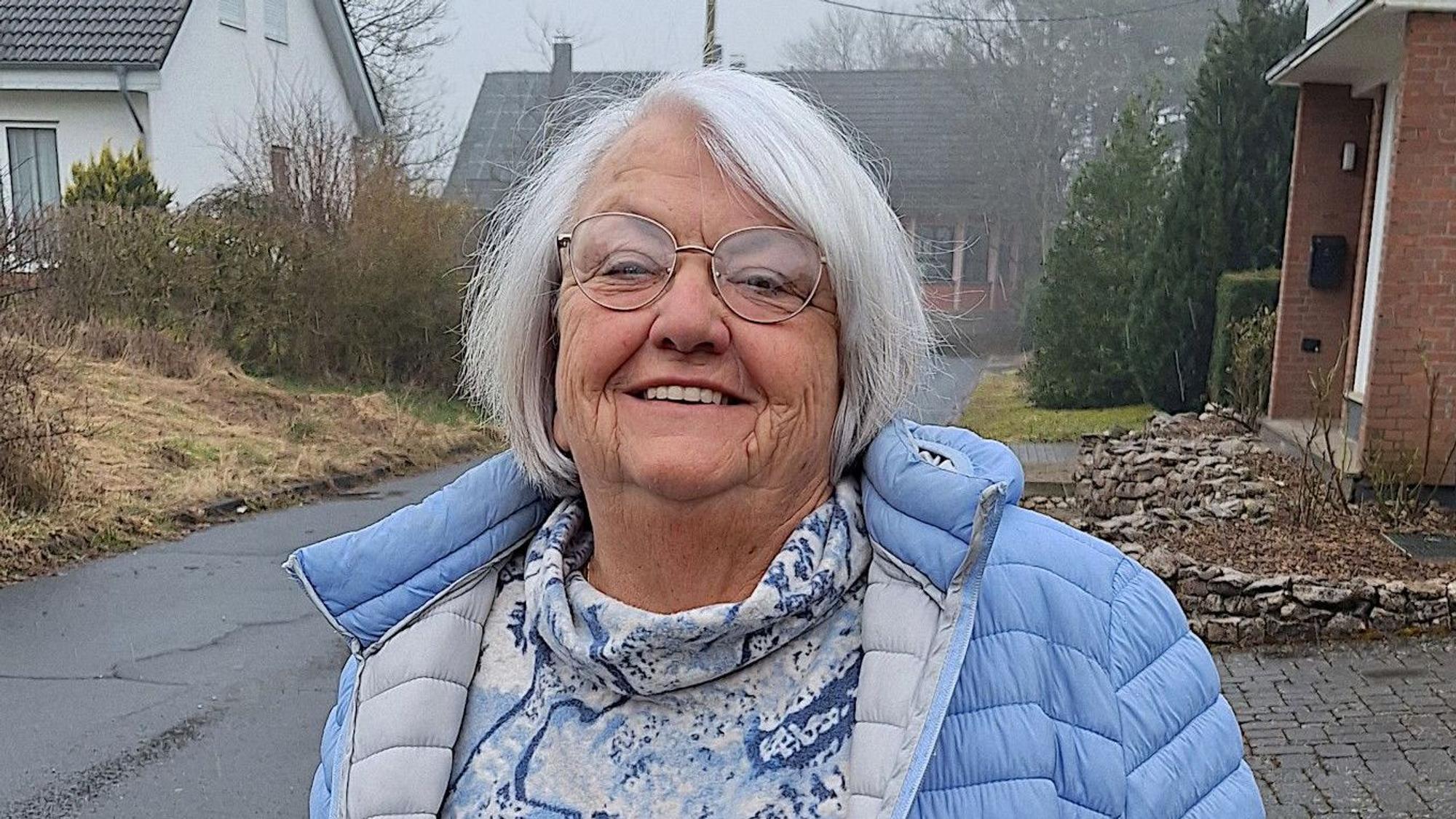 Eine Frau in blauer Jacke steht an einer Straße.