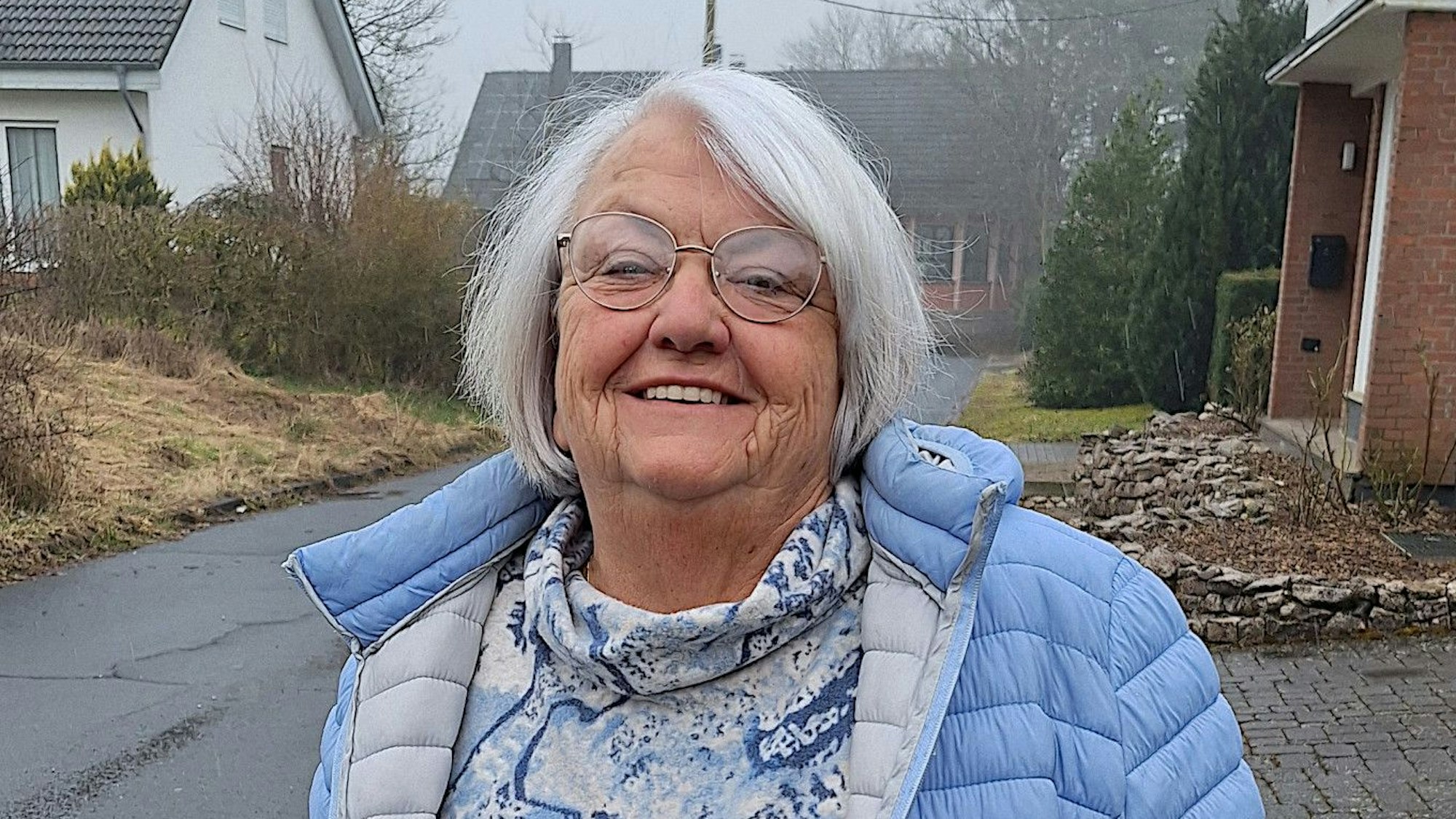 Eine Frau in blauer Jacke steht an einer Straße.