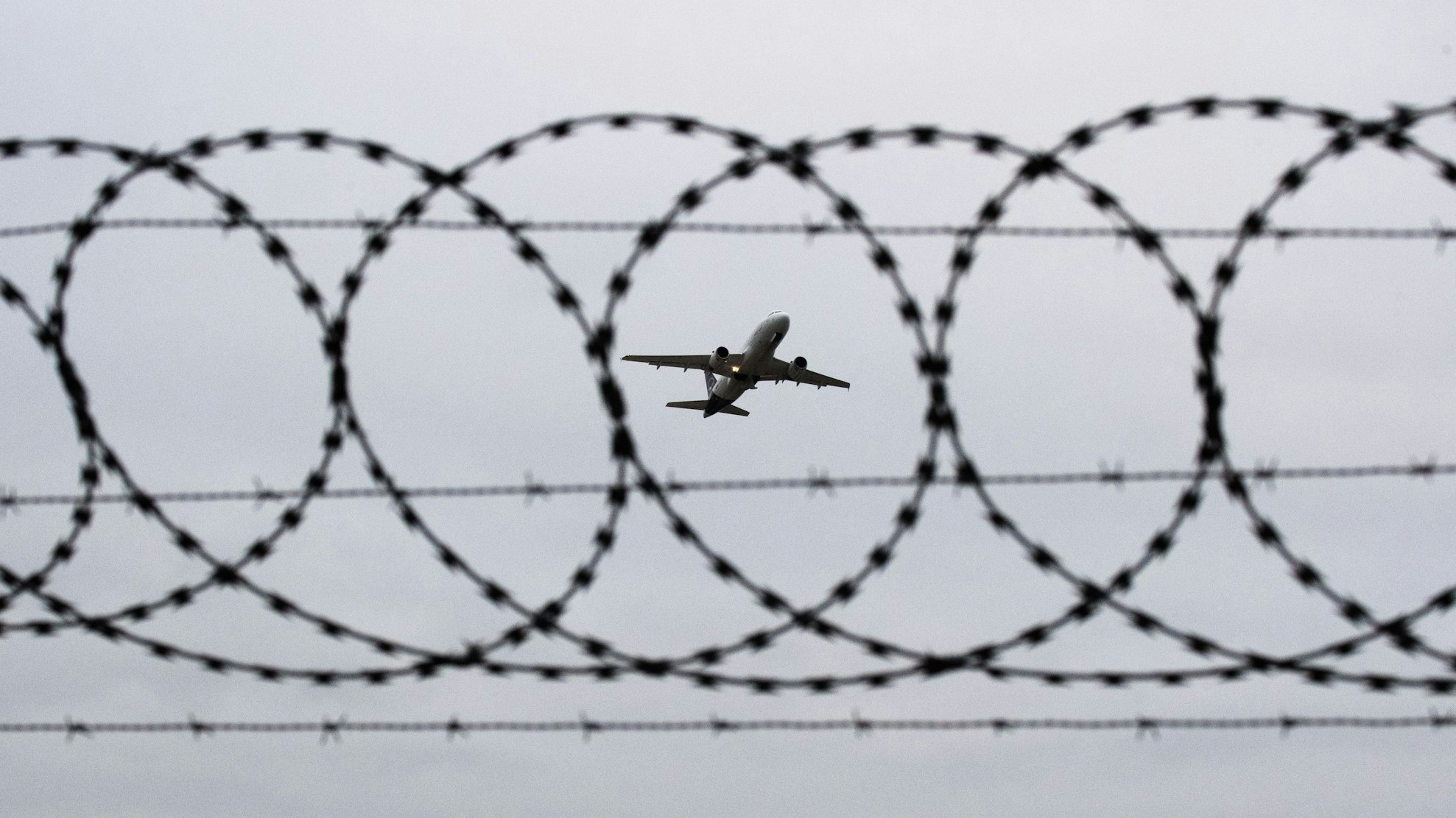 Ein Flugzeug startet - fotografiert durch einen Stacheldraht an einem Flughafenzaun.