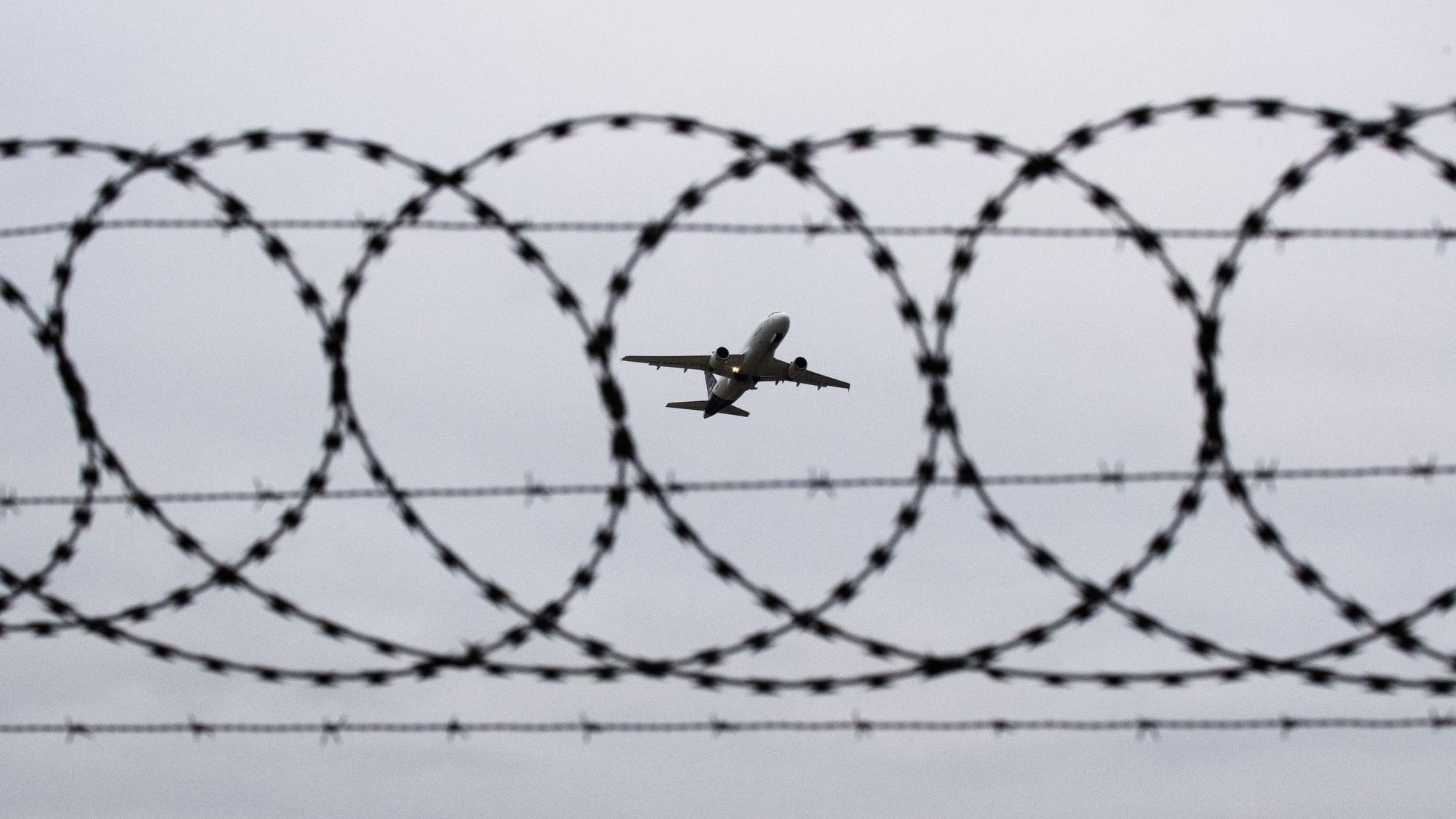 Ein Flugzeug startet - fotografiert durch einen Stacheldraht an einem Flughafenzaun.