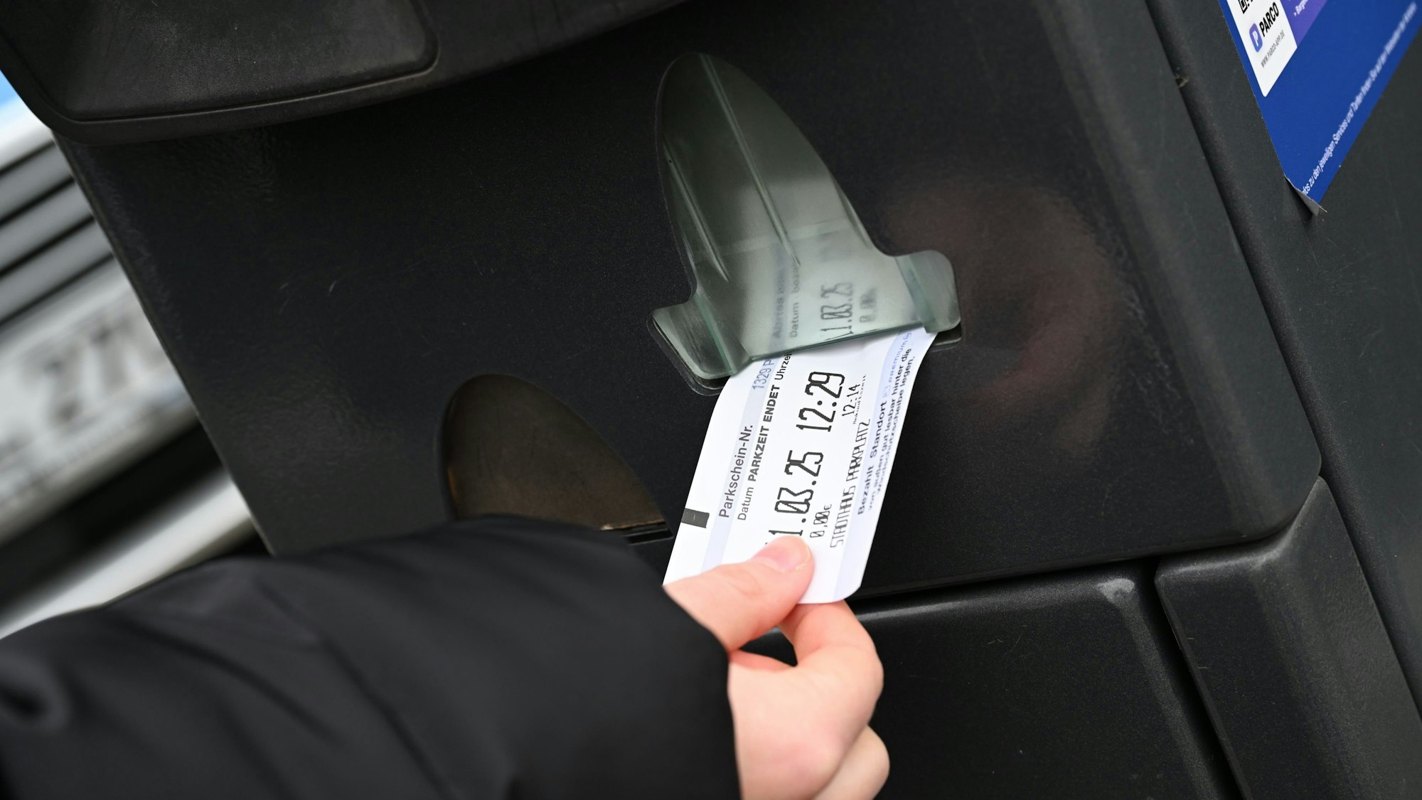 Man sieht, wie eine Hand einen Parkschein aus dem Automaten zieht.