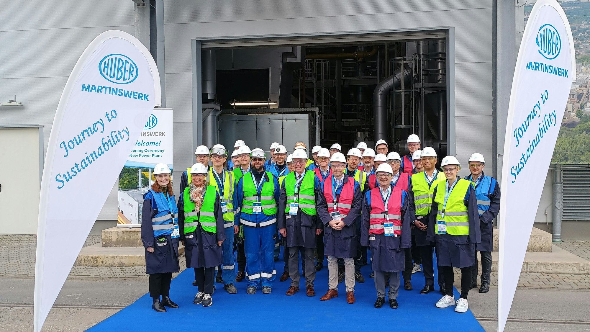 Menschen in Warnwesten und mit Helmen stehen vor einem Gebäude.