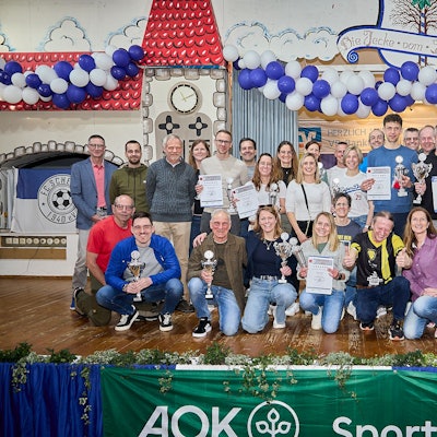 Zahlreiche Frauen und Männer stehen und hocken auf der Bühne im Dorfsaal in Scheven. Sie halten Pokale und Urkunden in den Händen, die sie beim Eifelcup gewonnen haben.