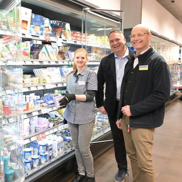 Eine Frau und zwei Männer stehen in einem Supermarkt vor einem Kühlregal mit Milchprodukten.