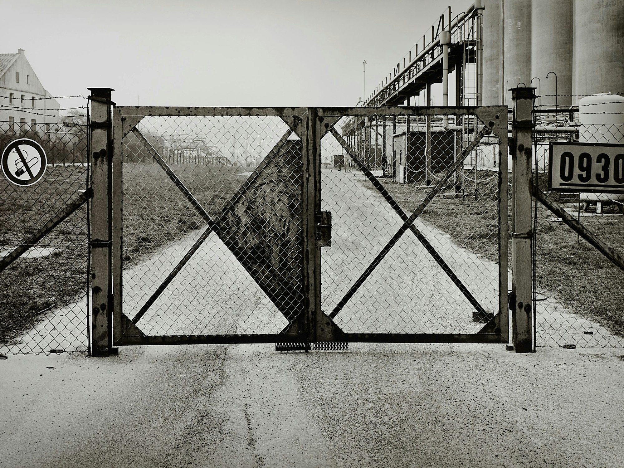 Ein Fabriktor steht vor einer Straße und Silos.