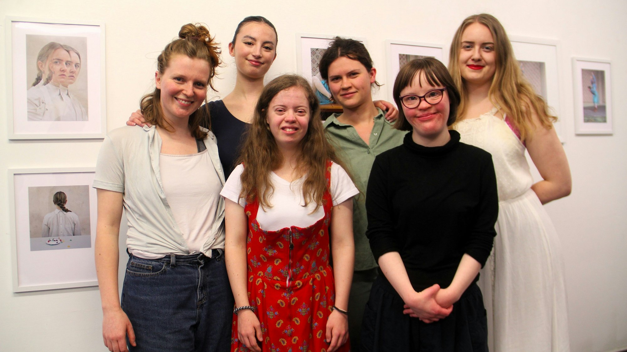 Sechs junge Frauen stehen vor einer Wand mit Bildern