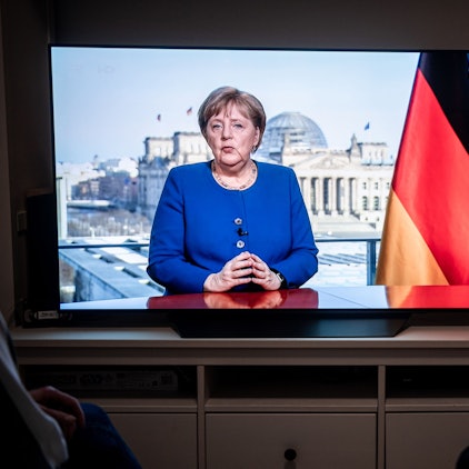 Das Bild zeigt Menschen, die der TV-Ansprache der Bundeskanzlerin Angela Merkel (CDU) in einem Wohnzimmer zusehen. Foto: Fabian Strauch/dpa