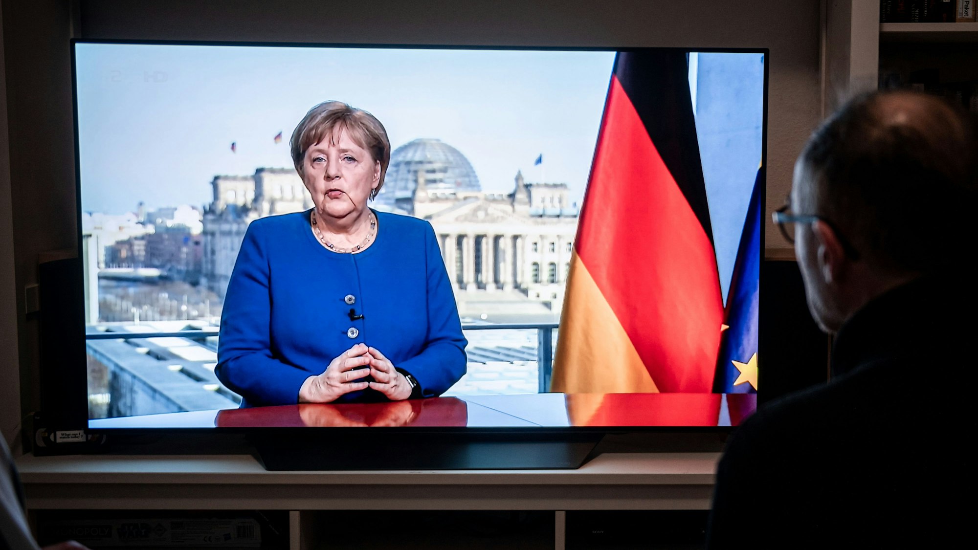 Das Bild zeigt Menschen, die der TV-Ansprache der Bundeskanzlerin Angela Merkel (CDU) in einem Wohnzimmer zusehen. Foto: Fabian Strauch/dpa
