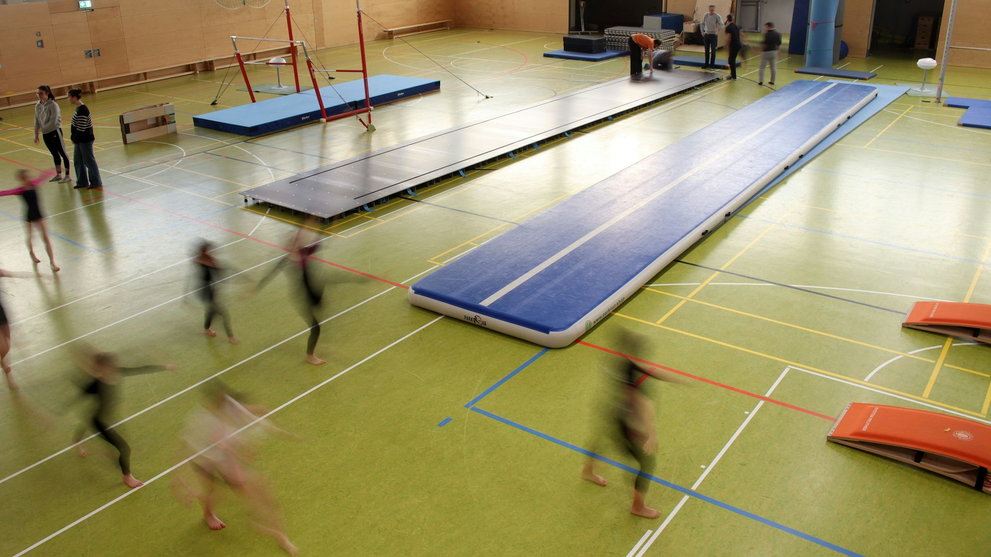 Während im Hintergrund die Gerätschaften aufgebaut werden, machen sich im Vordergrund die Turnerinnen, die bewusst unscharf sind, warm.