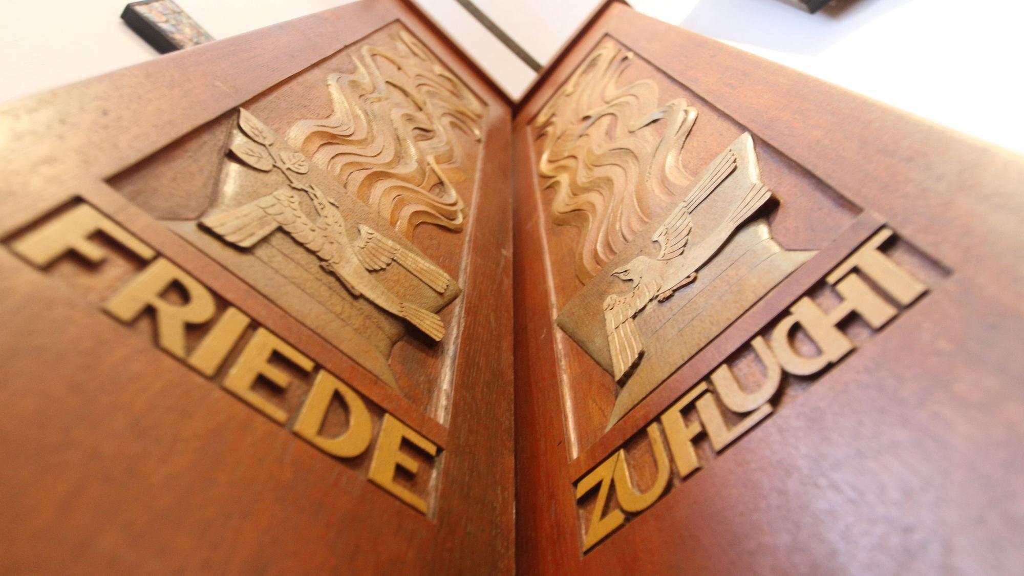 Zwei Holzbretter, eingeschnitzt sind die Wörter Friede und Zuflucht.