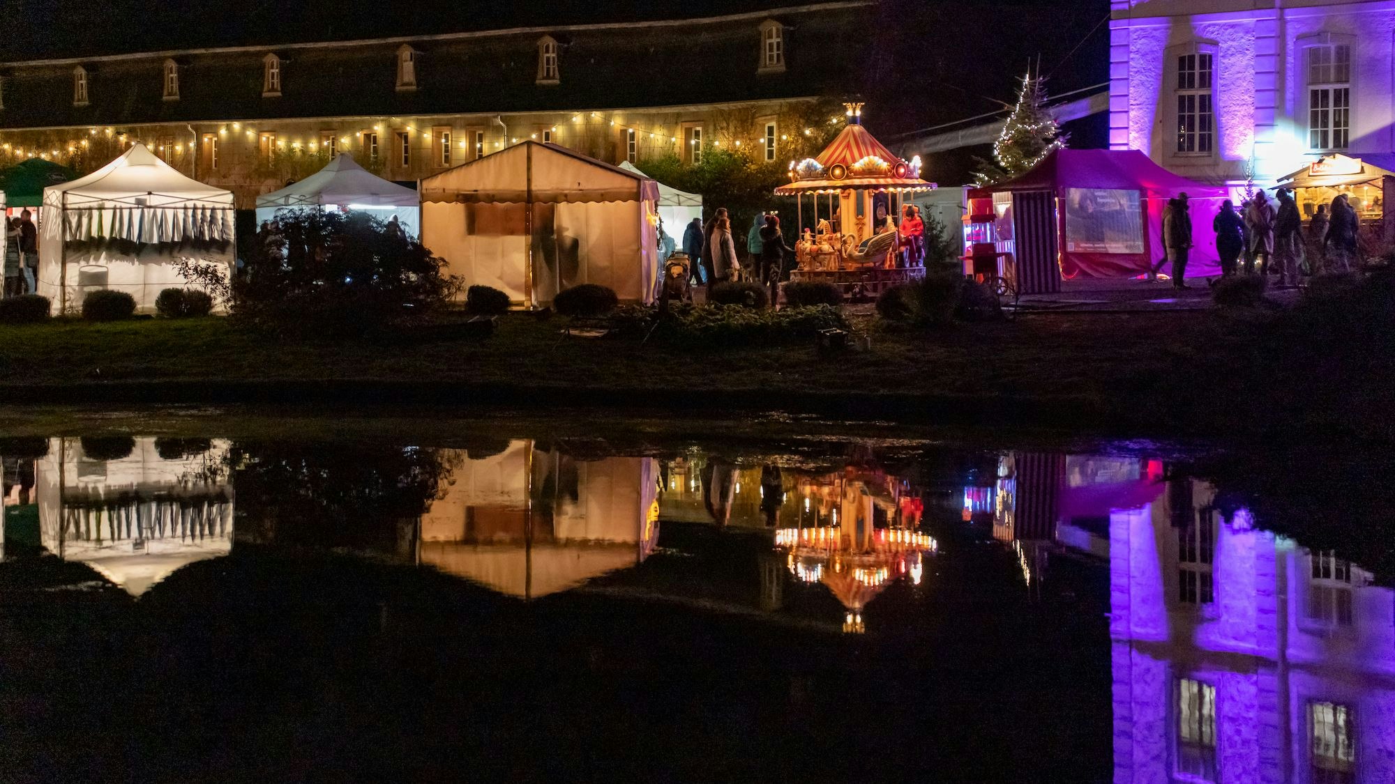 Verkaufsstände, die golden, weiß und lila beleuchtet sind, stehen vor dem Schloss Türnich.