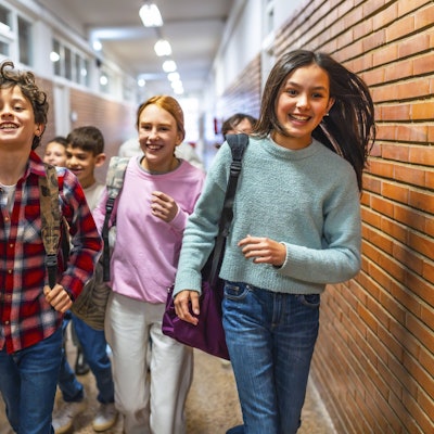 Fröhliche Schülerinnen und Schüler laufen lachend und aufgeregt durch den Schulflur.
