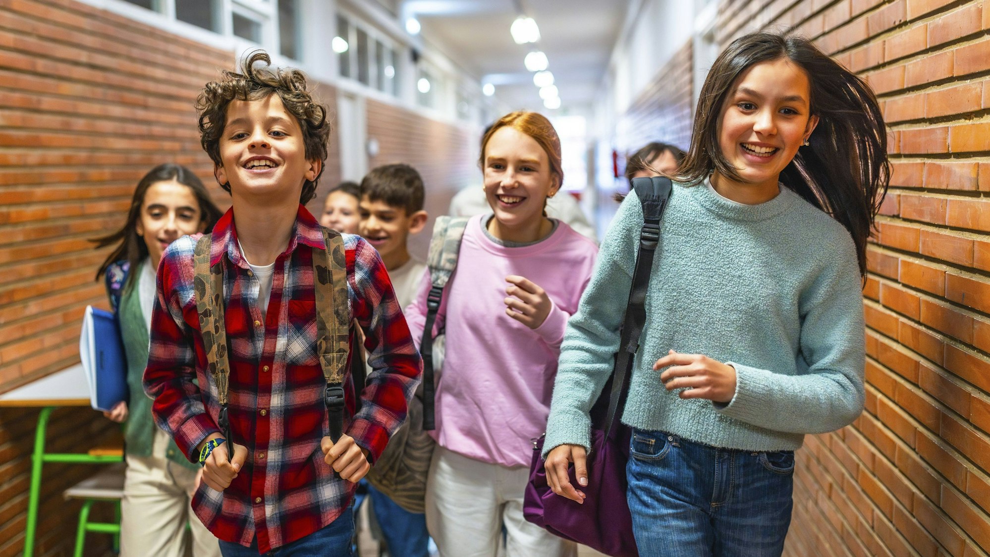 Fröhliche Schülerinnen und Schüler laufen lachend und aufgeregt durch den Schulflur.