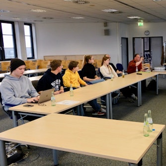 Jugendliche und Erwachsene sitzen in einem Sitzungssaal an Tischen zusammen.