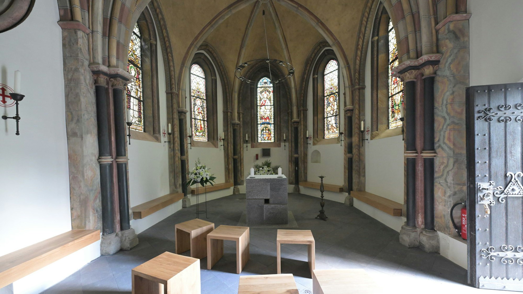 Eine kleine romanische Kapelle mit modernem Altar und Sitzhockern. Die Tür ist geöffnet.