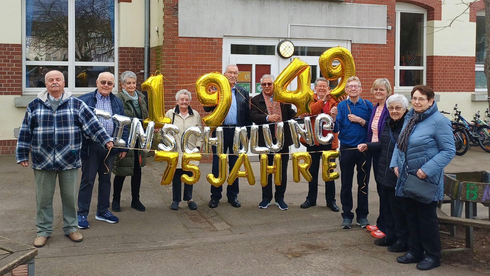 Menschen halten Luftballons hoch vor einer Schule.
