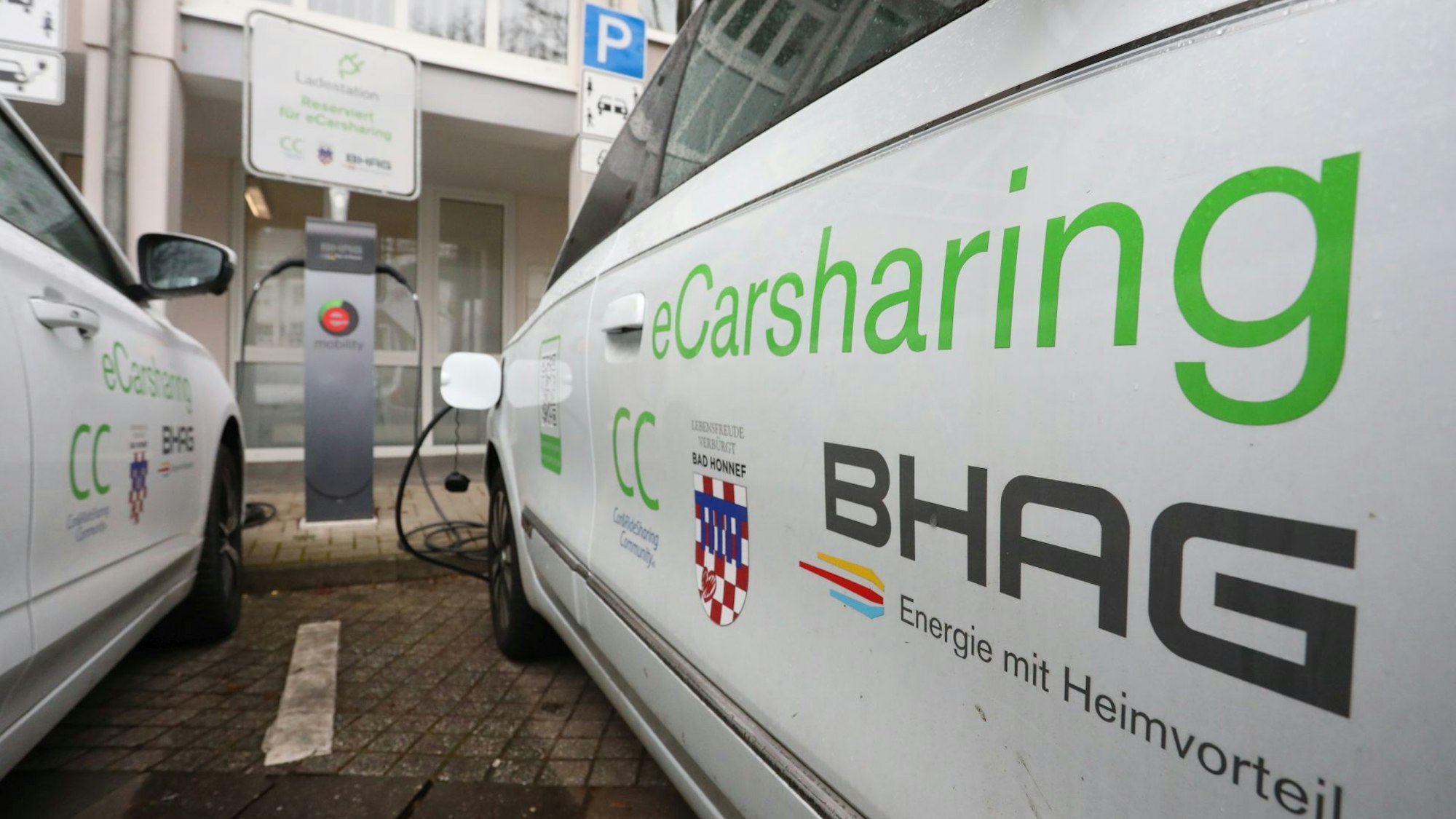 Zwei weiße Pkw mit der Aufschrift E-Carsharing vor einer Ladestation.
