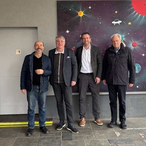 Vier Männer stehen vor einem gemalten Weltraumbild