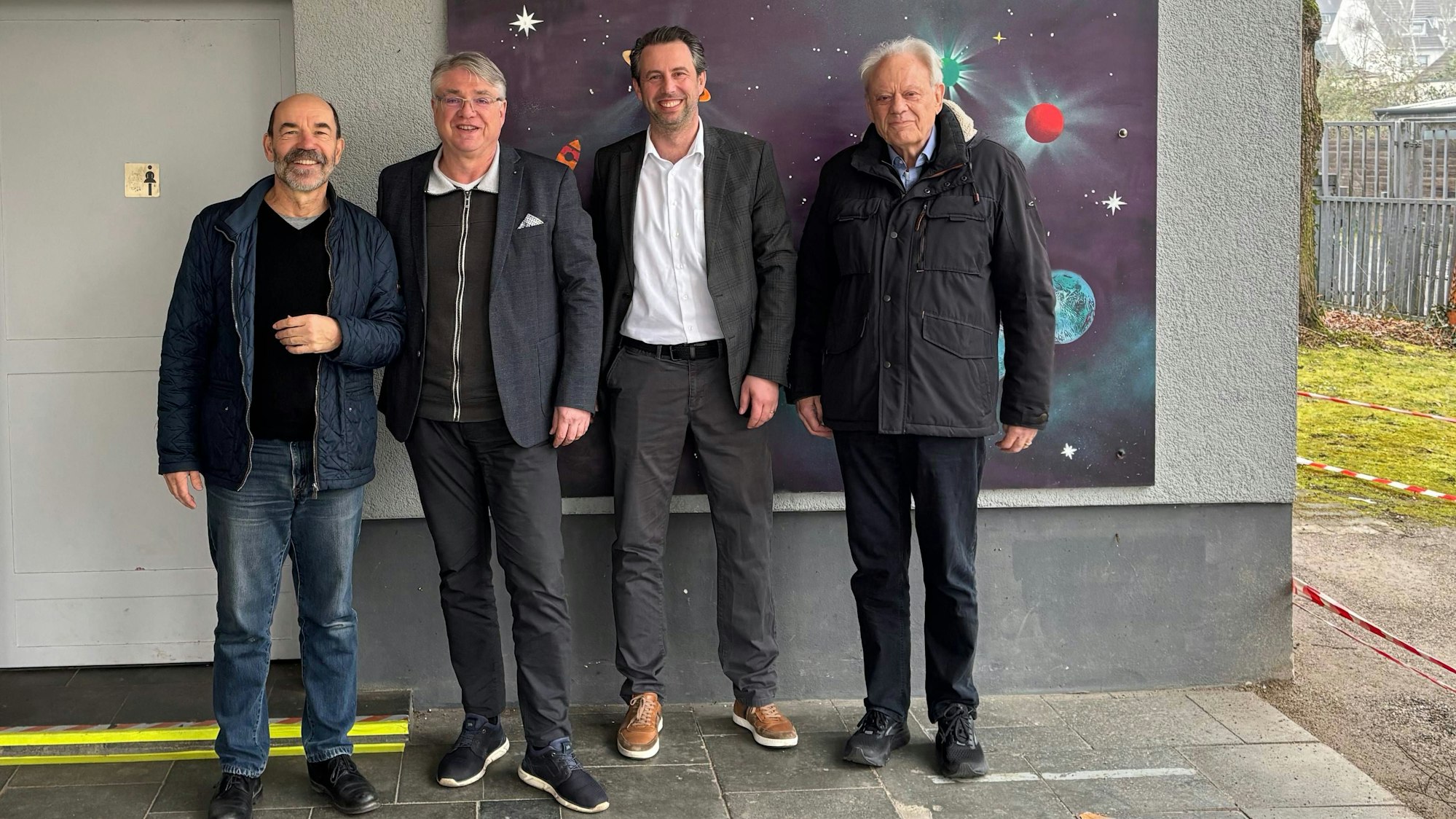 Vier Männer stehen vor einem gemalten Weltraumbild
