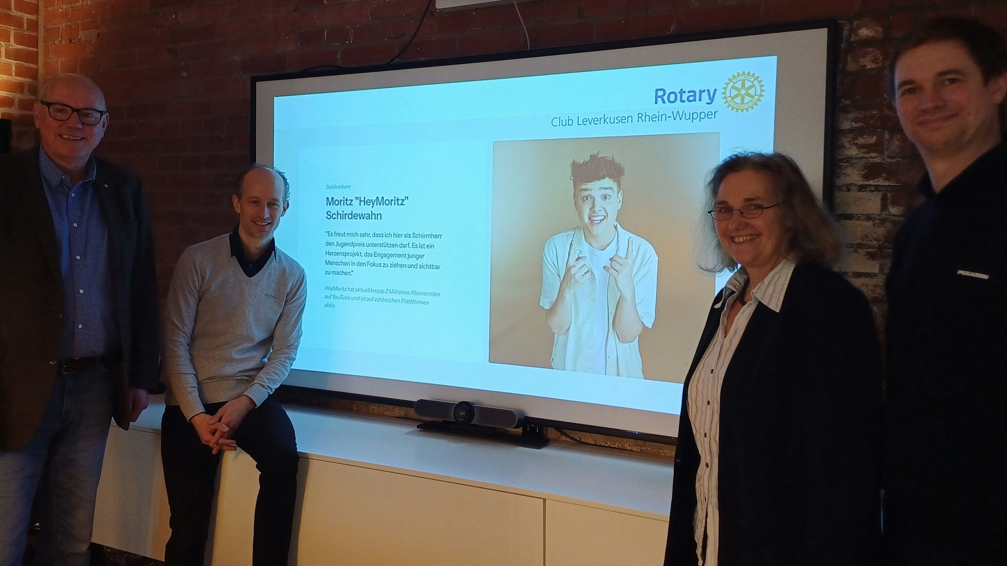 Vier Personen stehen vor einem Bildschirm.