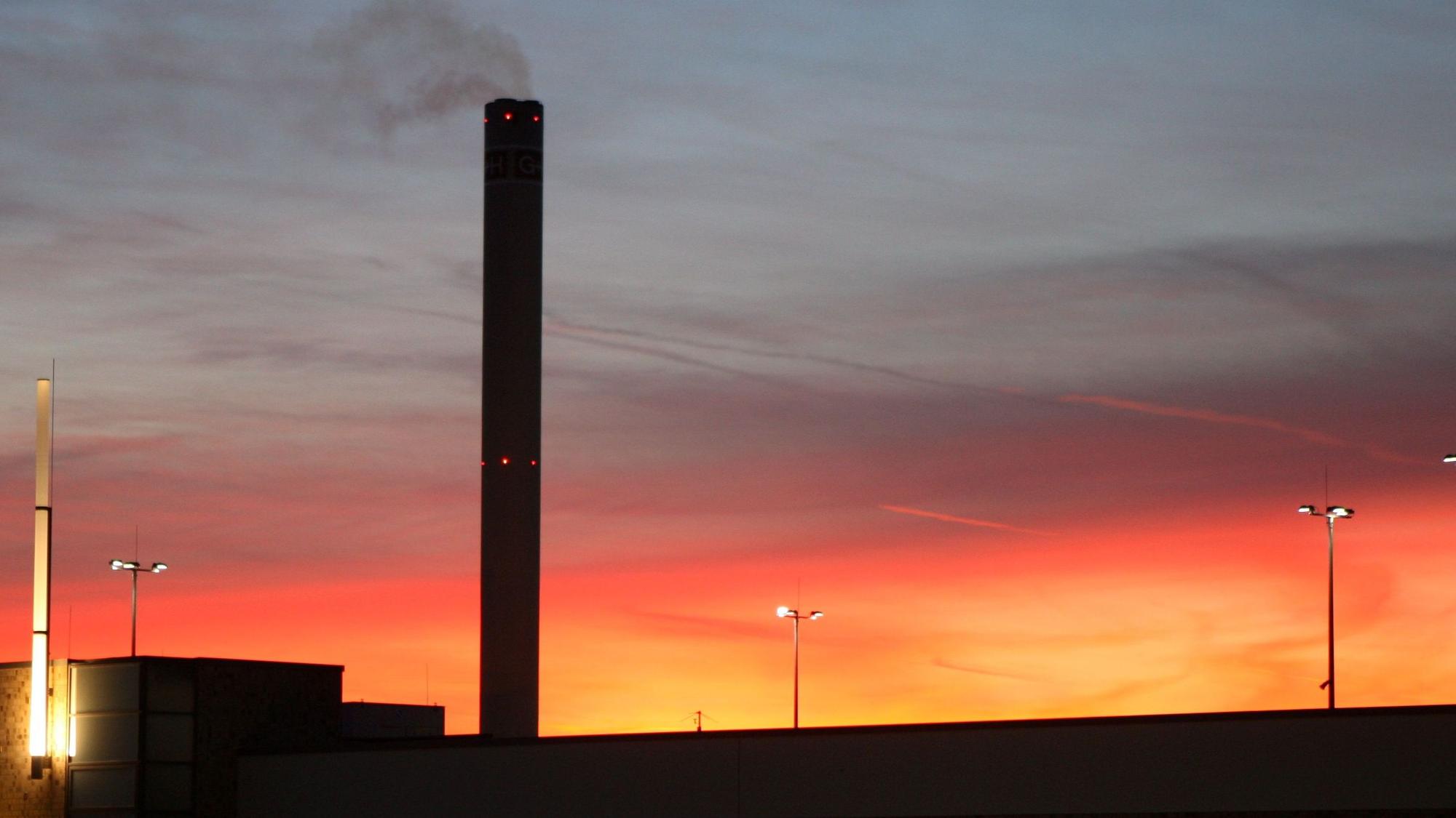 Der Schornstein des Isover-Werks in Bergisch Gladbach raucht vor dem Sonnenuntergangshimmel vor sich hin.