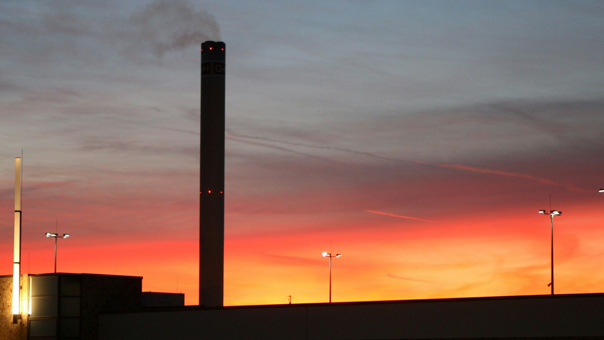 Der Schornstein des Isover-Werks in Bergisch Gladbach raucht vor dem Sonnenuntergangshimmel vor sich hin.